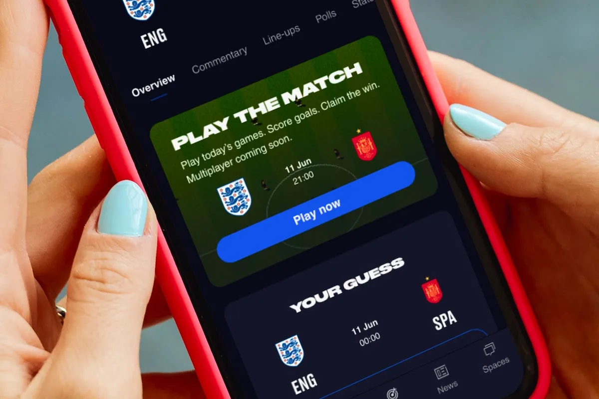 A hand holding a phone showing the Match Center for England vs Spain, with a Play the Match card and the fan's prediction