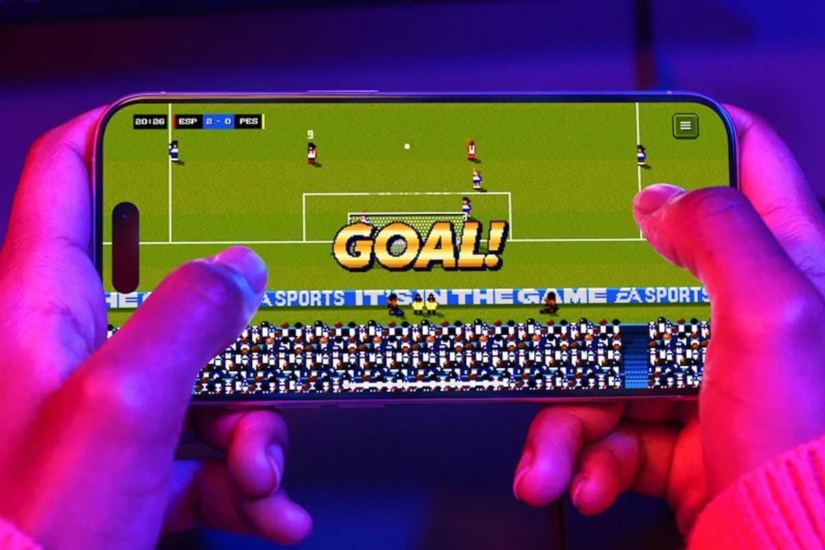 Hands holding a phone in landscape, scoring a goal in the retro 16-bit Sensible Soccer revival inside the EA SPORTS App